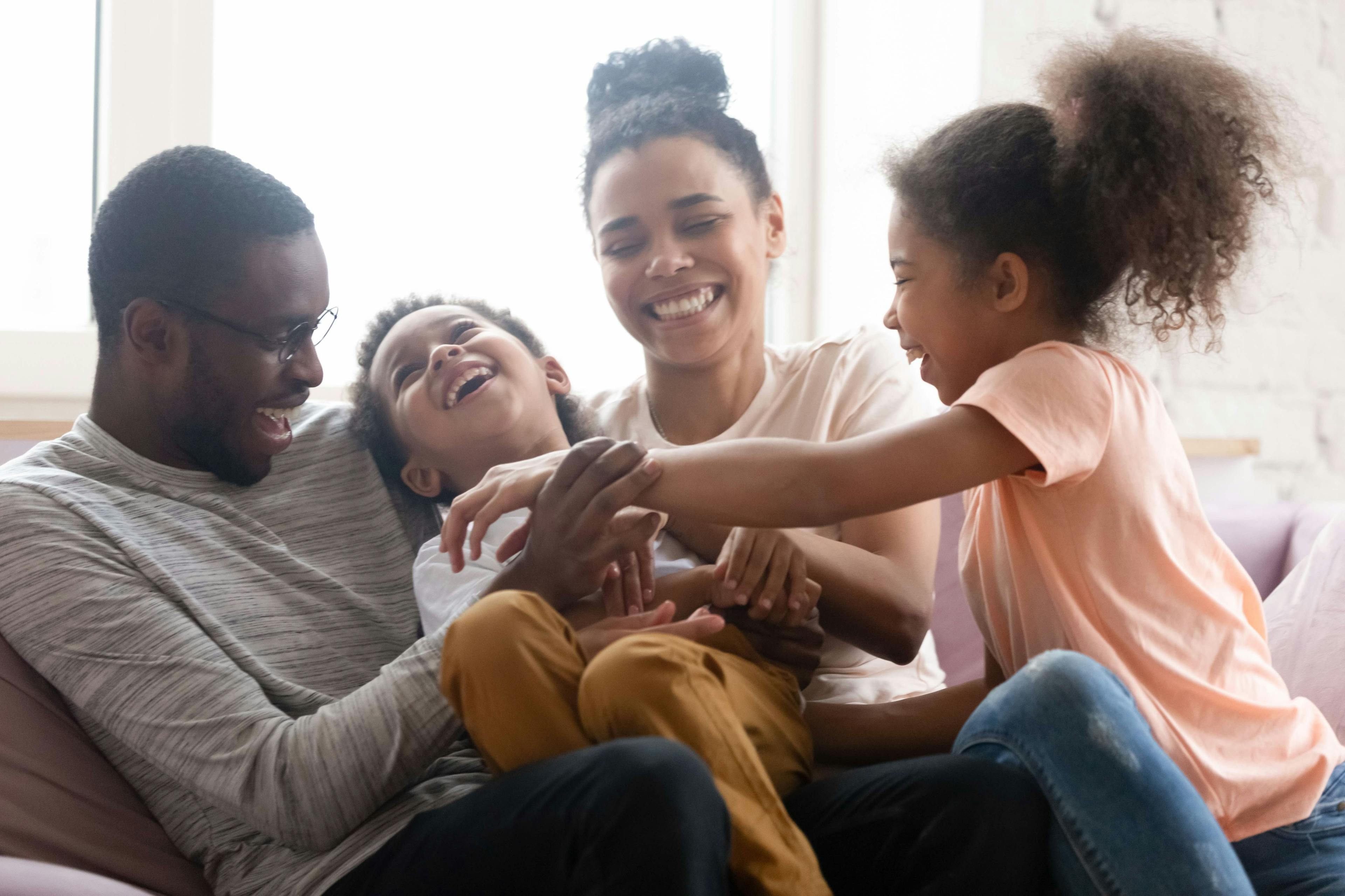 Black parents and two kids laughing on a couch