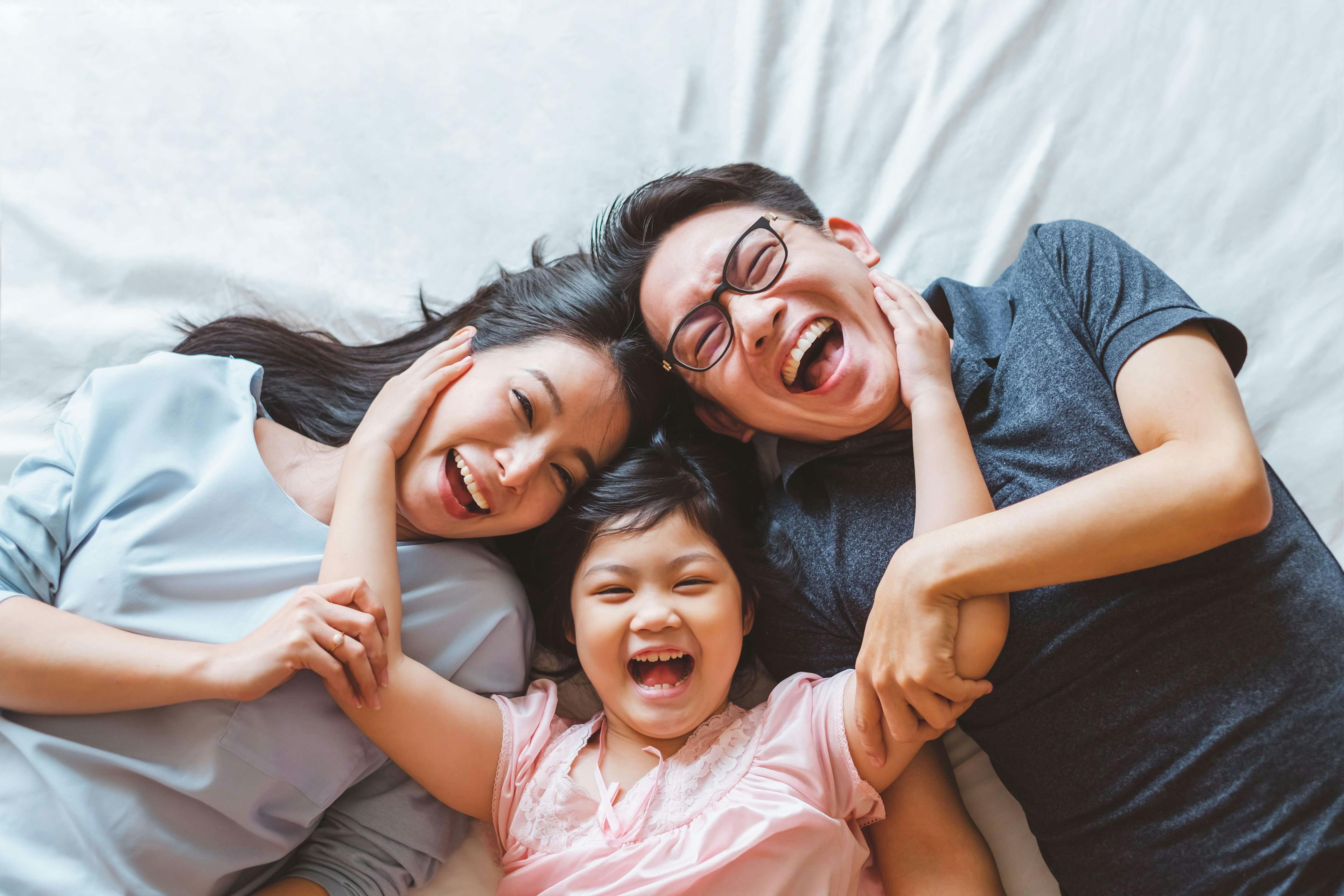 Asian parents with daughter laughing on a bed